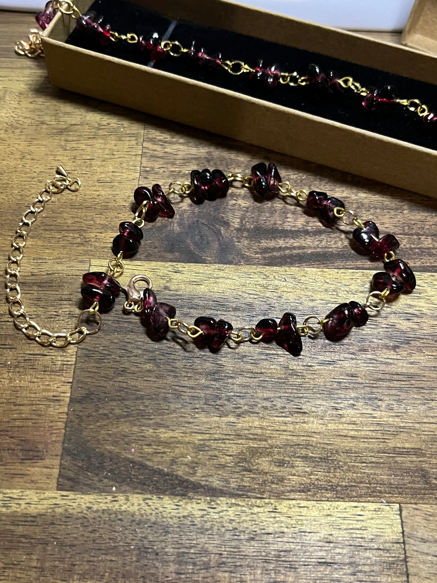 Necklace with burgundy beads and gold chain on a wooden surface